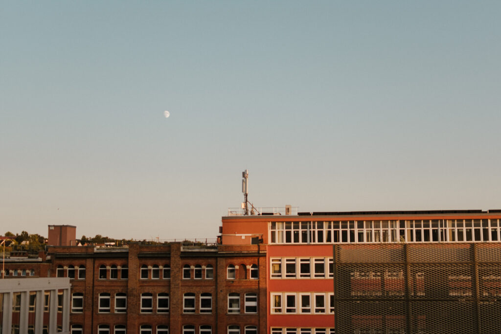 Photo of the evening sky overlooking some industrial buildings and the moon popping out in Würzburg, Germnay.